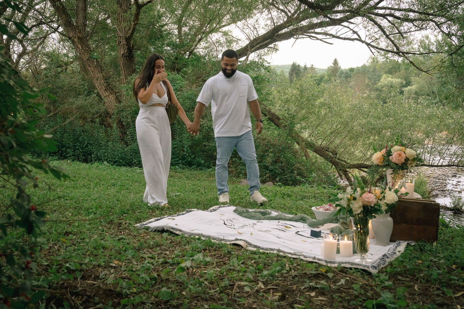 A romantic outdoor picnic setup in a lush garden with white blankets and floral arrangements in natural light.