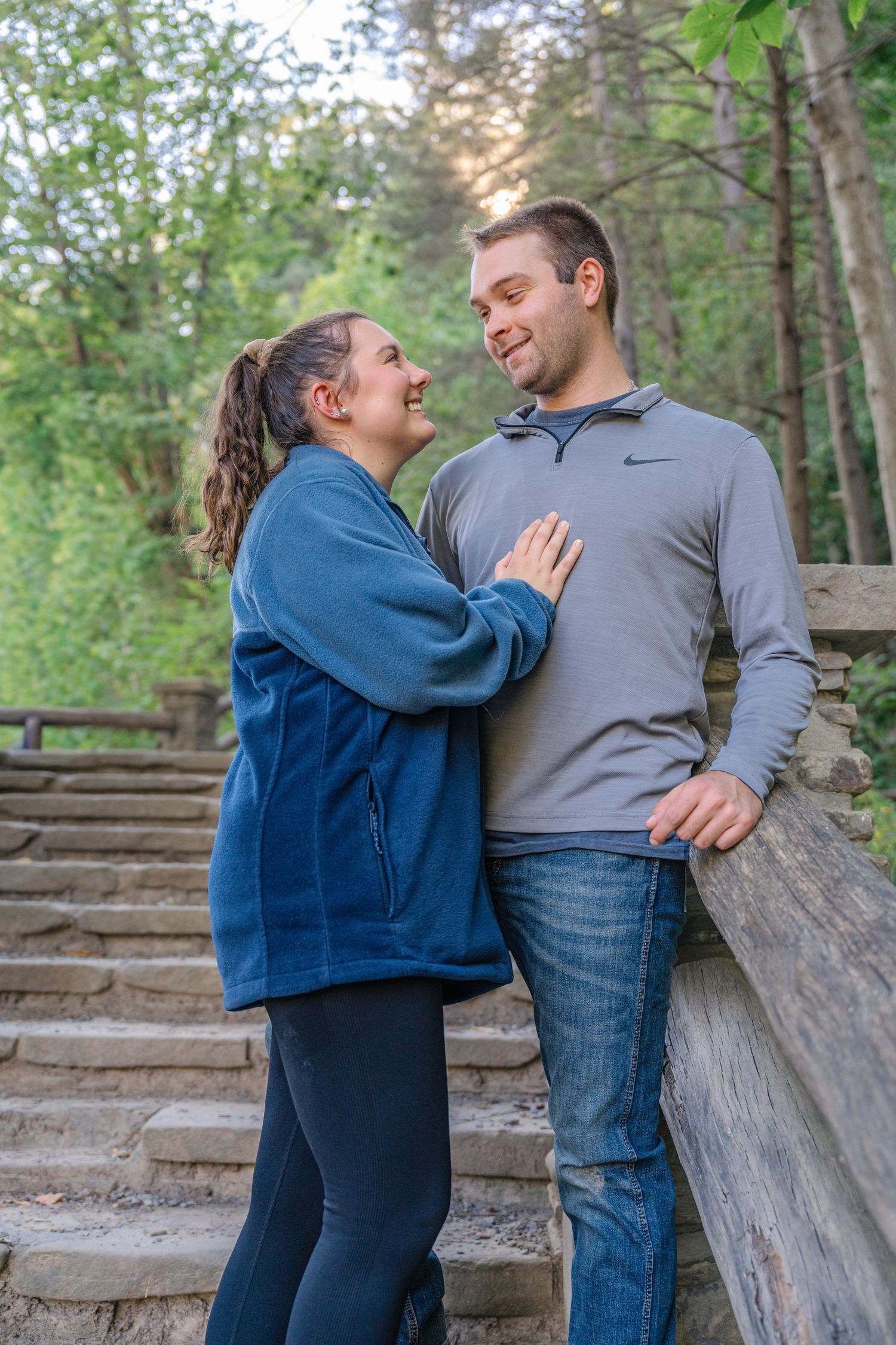 A couple shares a romantic moment together on stone steps in a wooded outdoor setting.