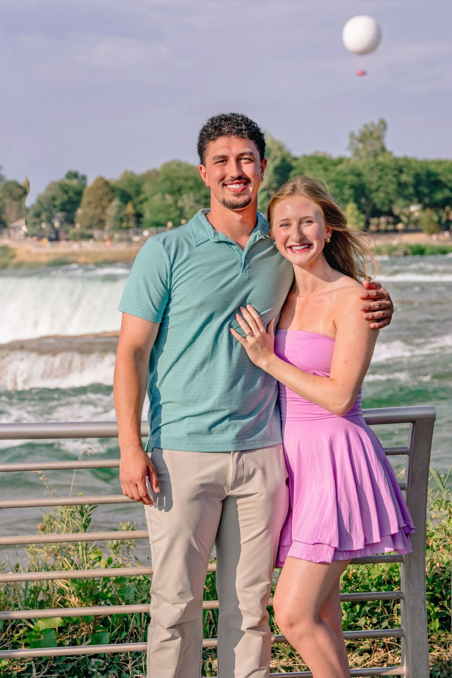 A couple shares a joyful moment near Niagara Falls with the waterfall visible in the background.