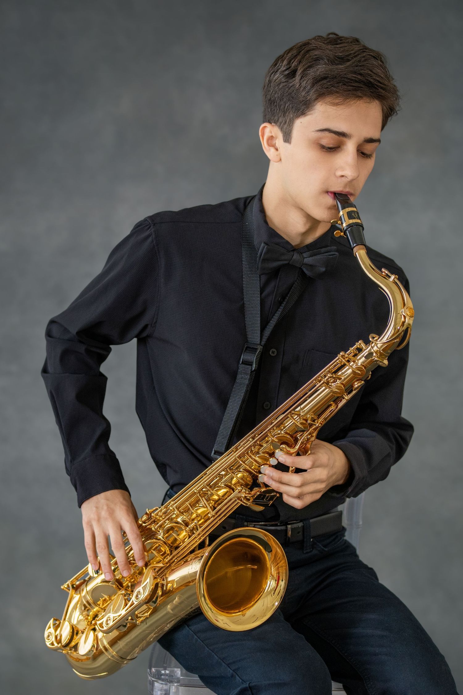 Saxophone player performs with golden instrument while wearing formal black clothing in studio setting.