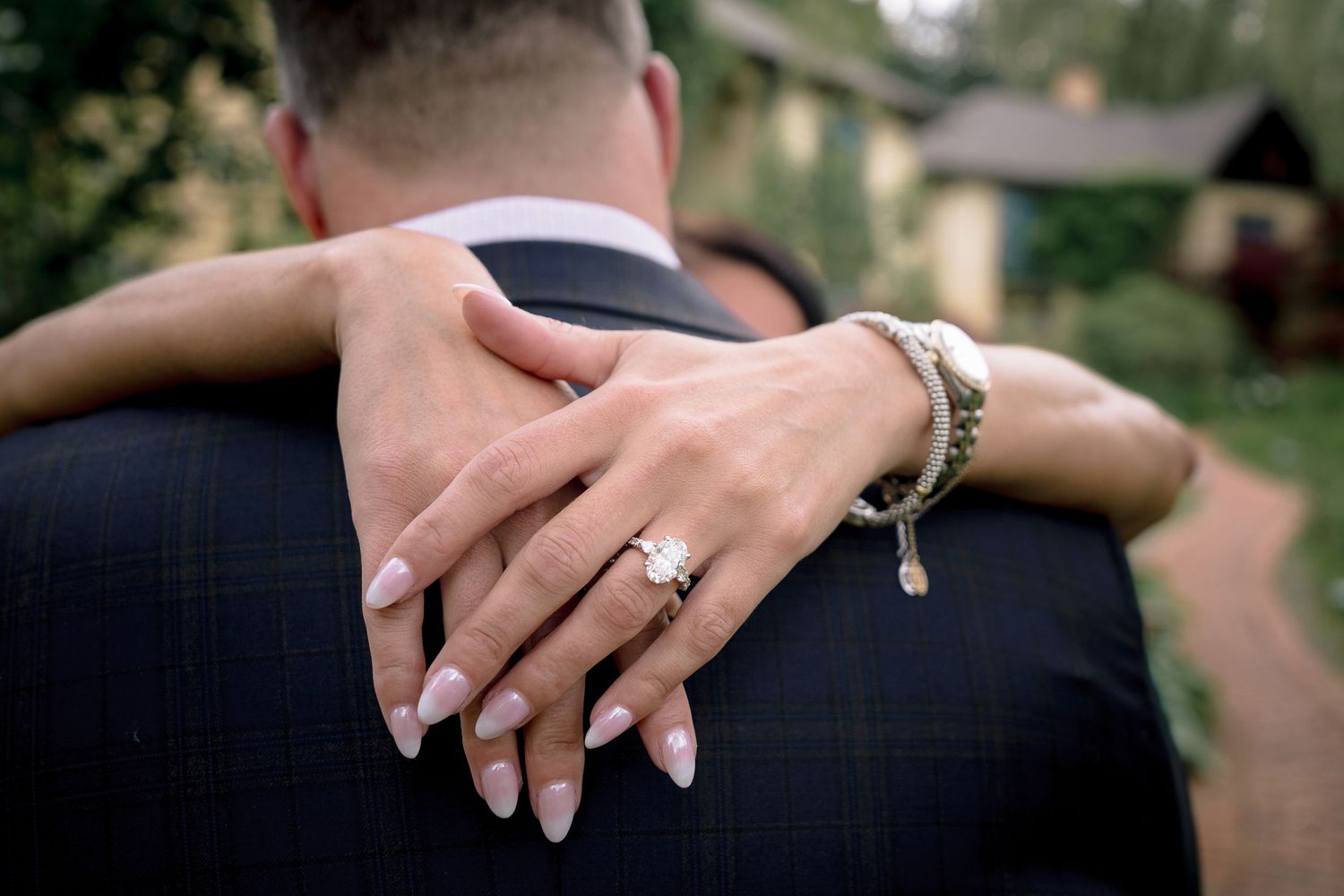 Close-up of hands with engagement ring embracing in a romantic outdoor setting.