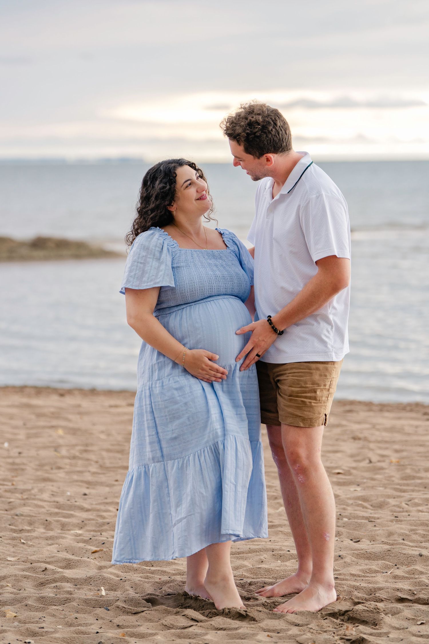 A mother and child share tender moments on a beach at sunset wearing matching light blue dresses.