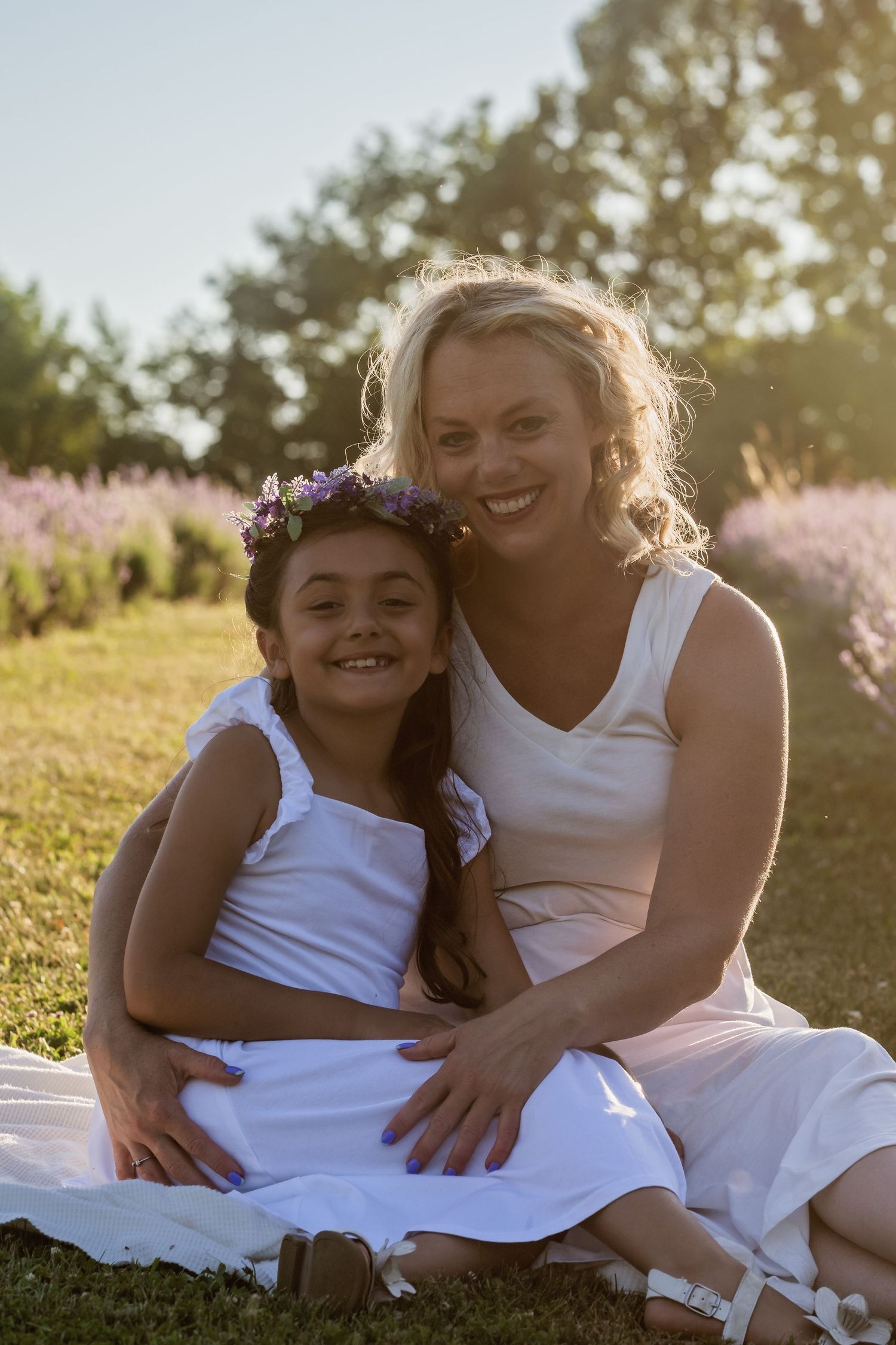 Two people in white dresses share tender moments while sitting together on grass during golden hour.