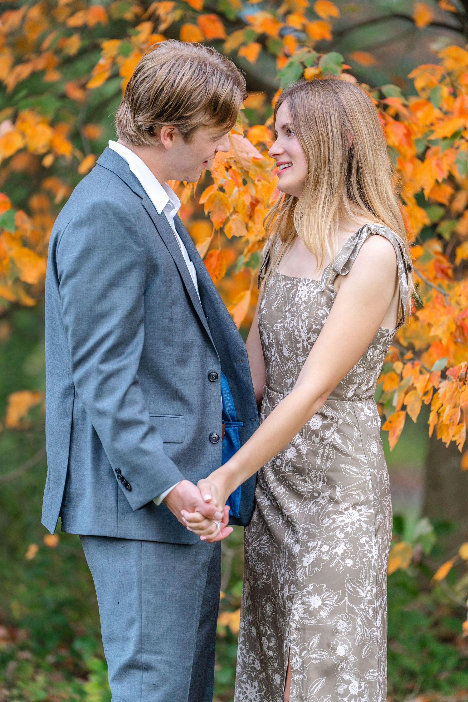A couple in formal attire shares a romantic moment against vibrant autumn foliage with orange maple leaves.