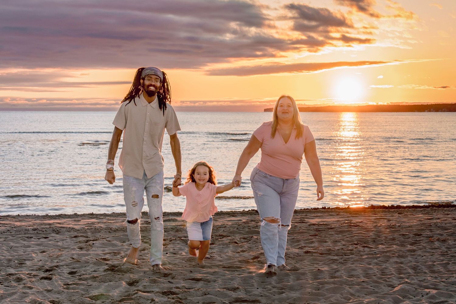 Family walking along shoreline during golden sunset with ocean waves in background.