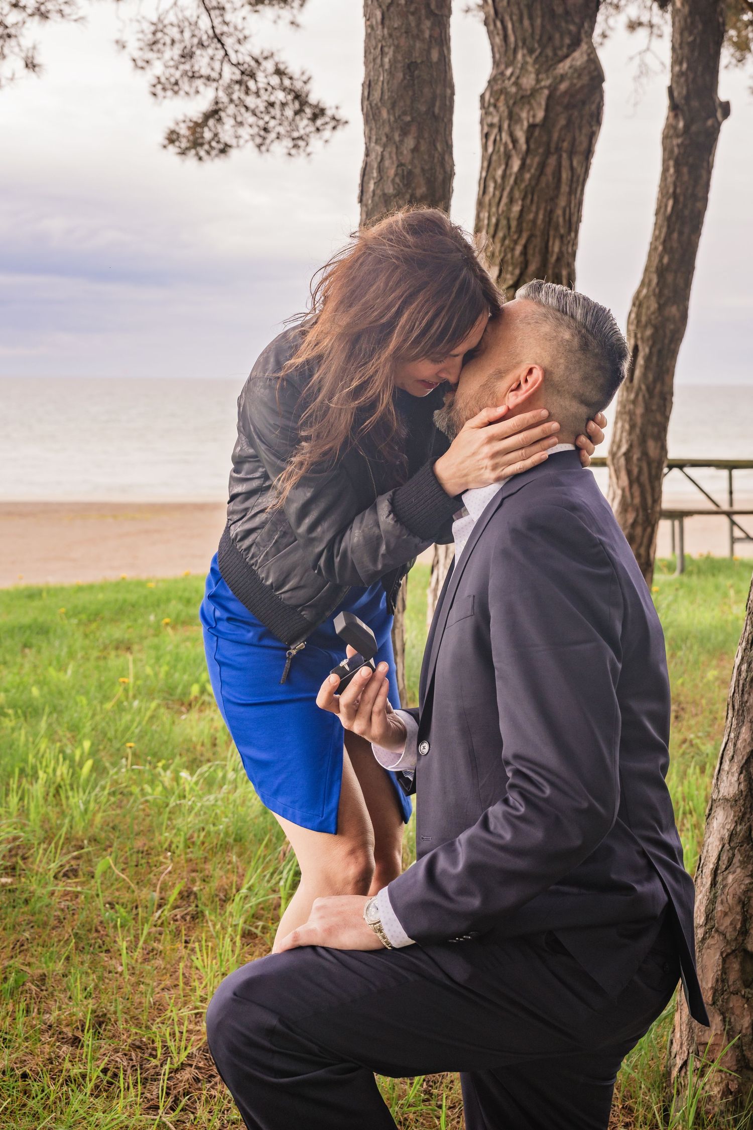 A romantic proposal sequence captured outdoors with trees and grass in the background.