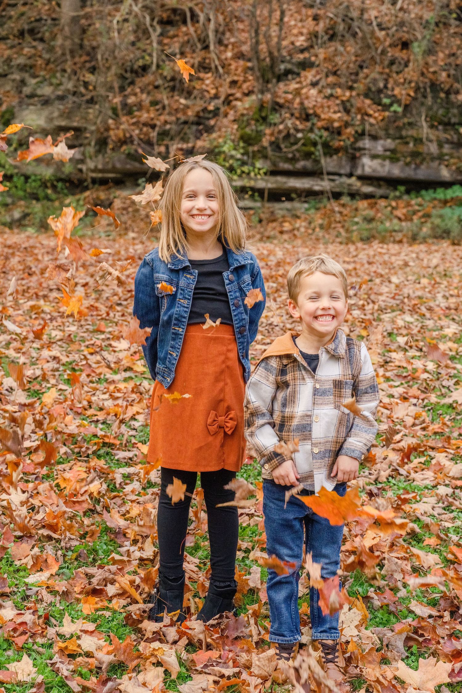 Two children play in a pile of fallen autumn leaves on a crisp fall day.