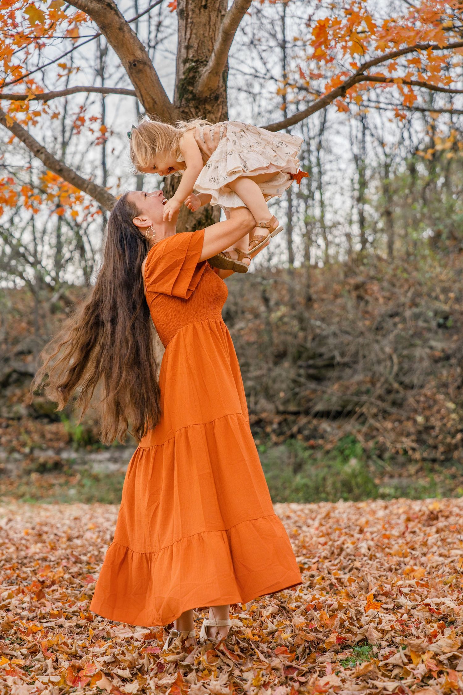 Dancing figure in bright orange dress twirls joyfully among autumn leaves in a forest setting.