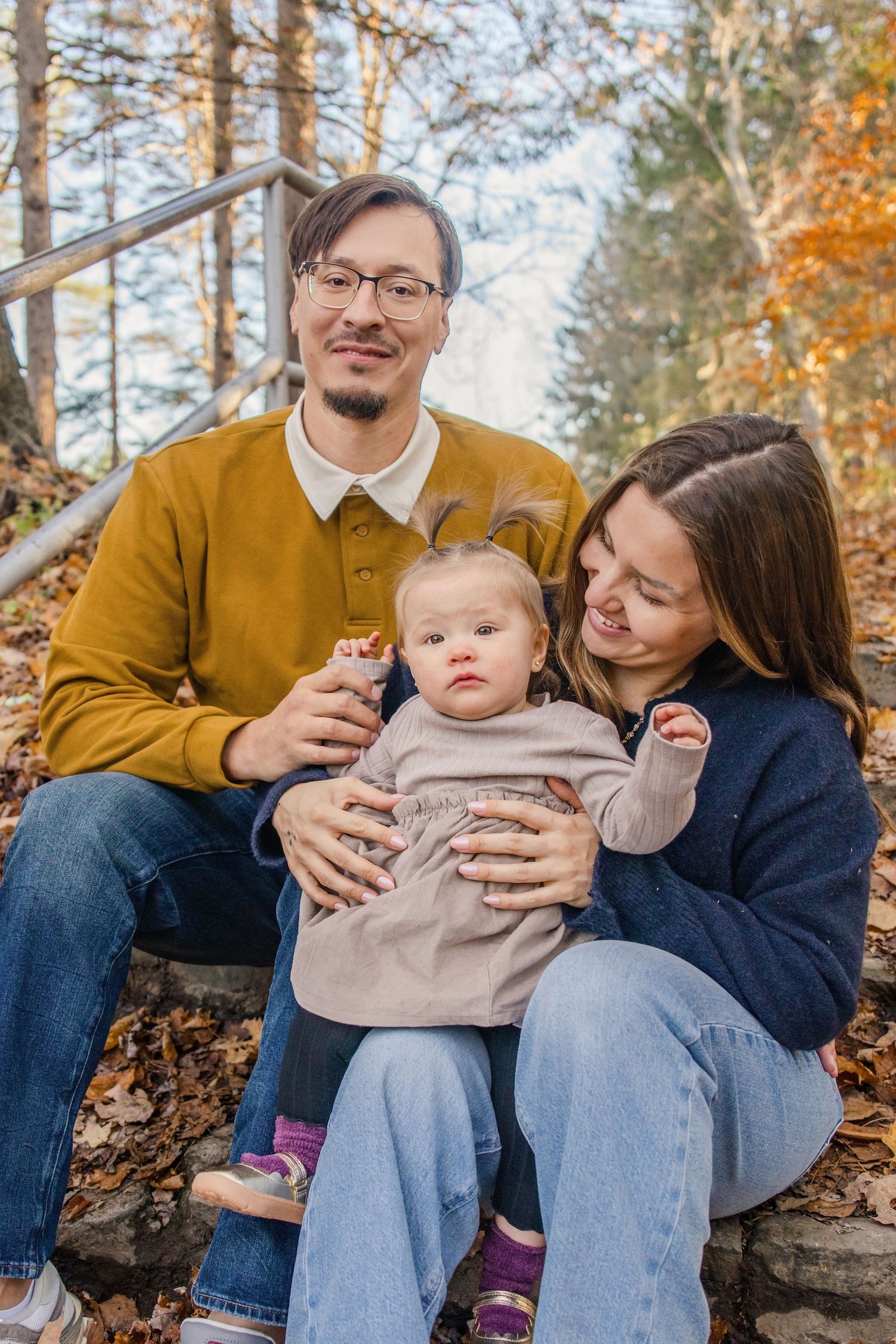 A family sits together on stone steps surrounded by fallen autumn leaves in a forest setting.