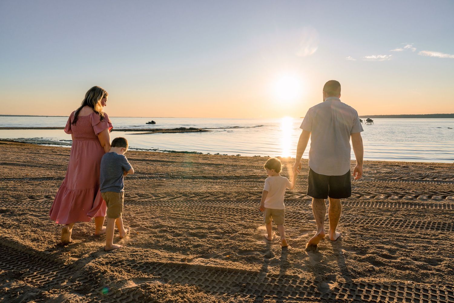 Silhouettes of people walking along a peaceful beach shoreline at sunset with calm waters in the background.