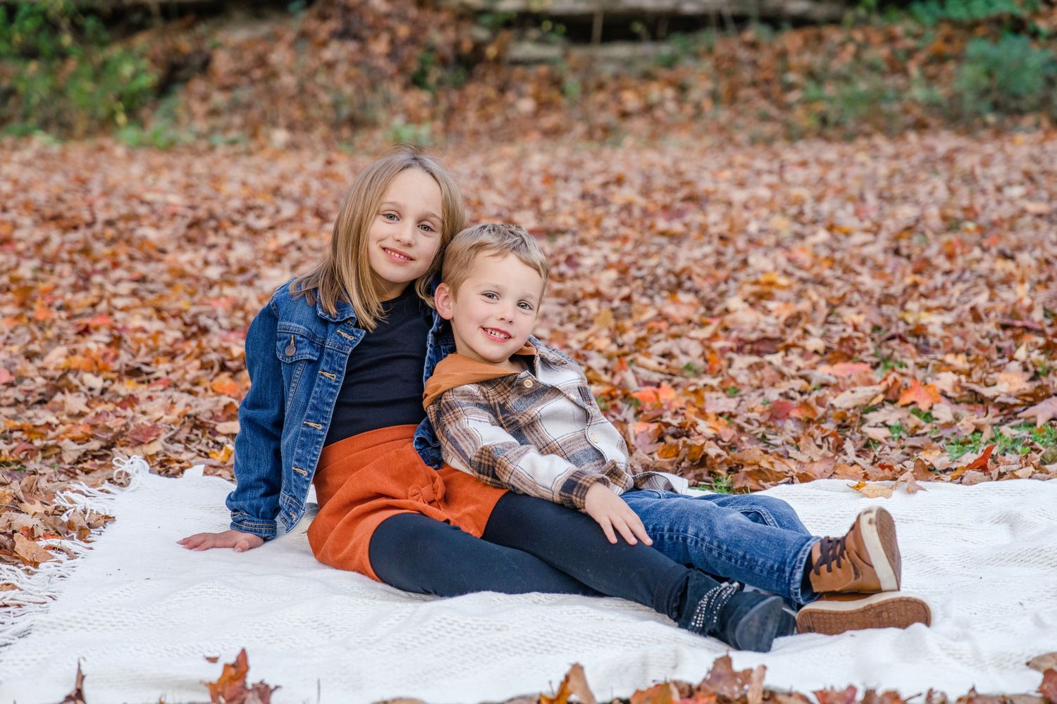 A group of autumn portraits taken on a blanket surrounded by fallen leaves in a park setting.