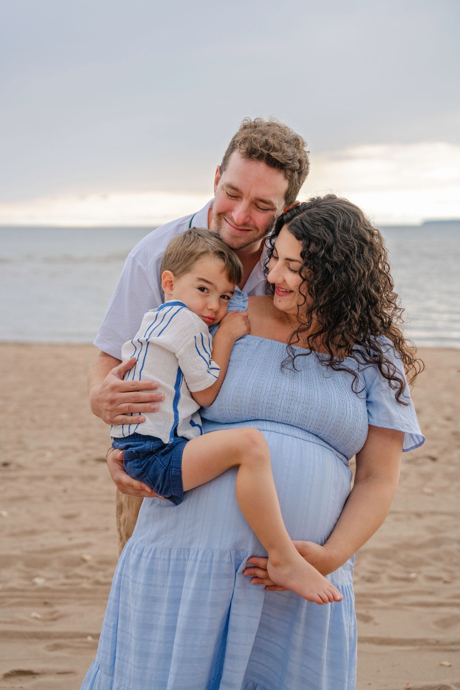 Family shares tender moment together on beach as sun sets over water in background.
