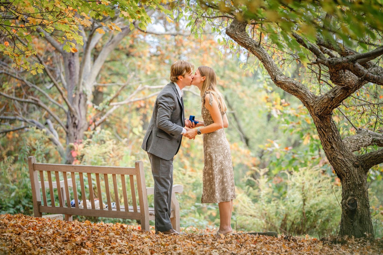 Couple embraces in romantic autumn garden setting surrounded by colorful fall foliage and trees.