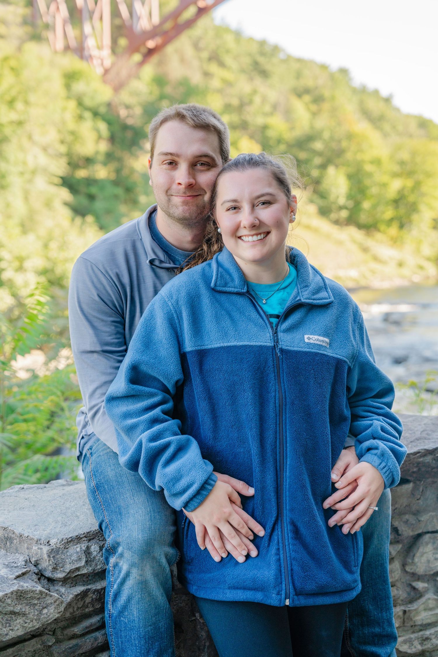 A couple sits together on stone steps surrounded by lush greenery on a sunny day.