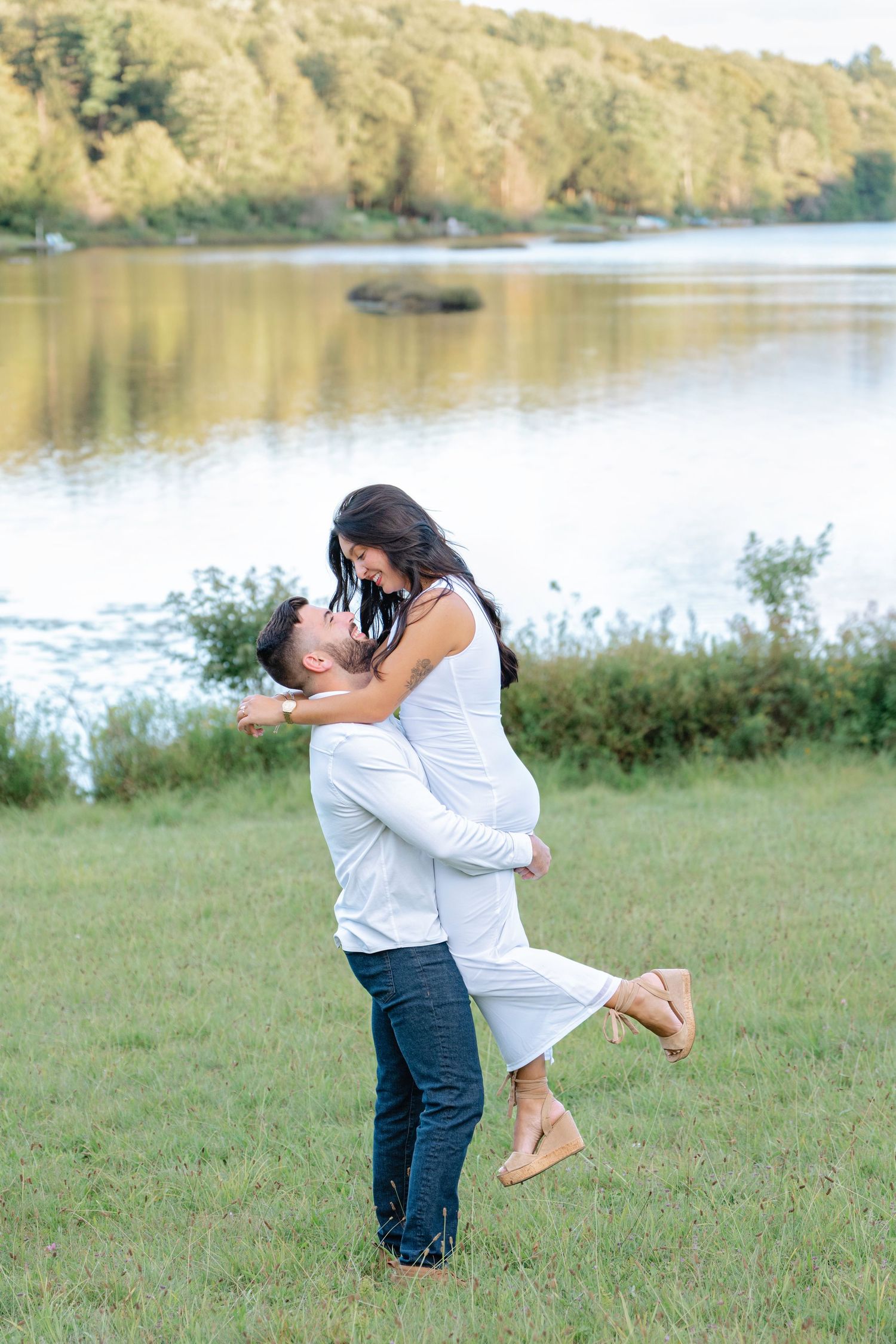 A romantic couple embraces by a serene lake with autumn trees in the background.