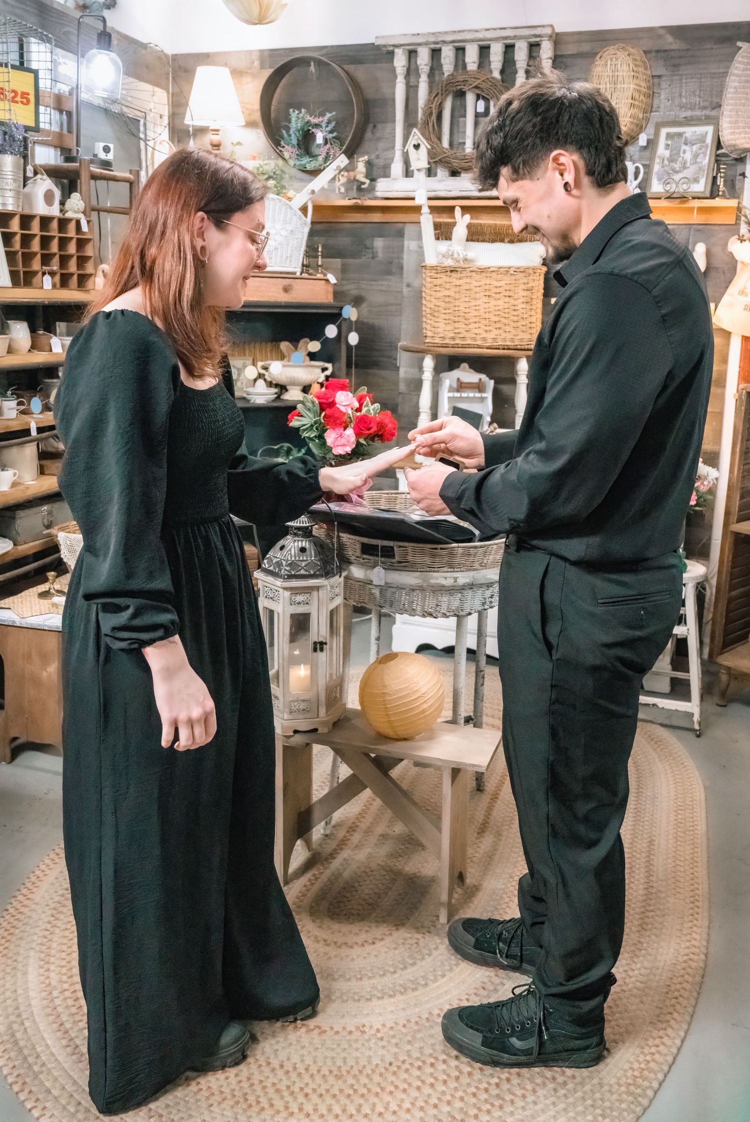 Couple in matching black outfits exchanging rings in a charming boutique shop.