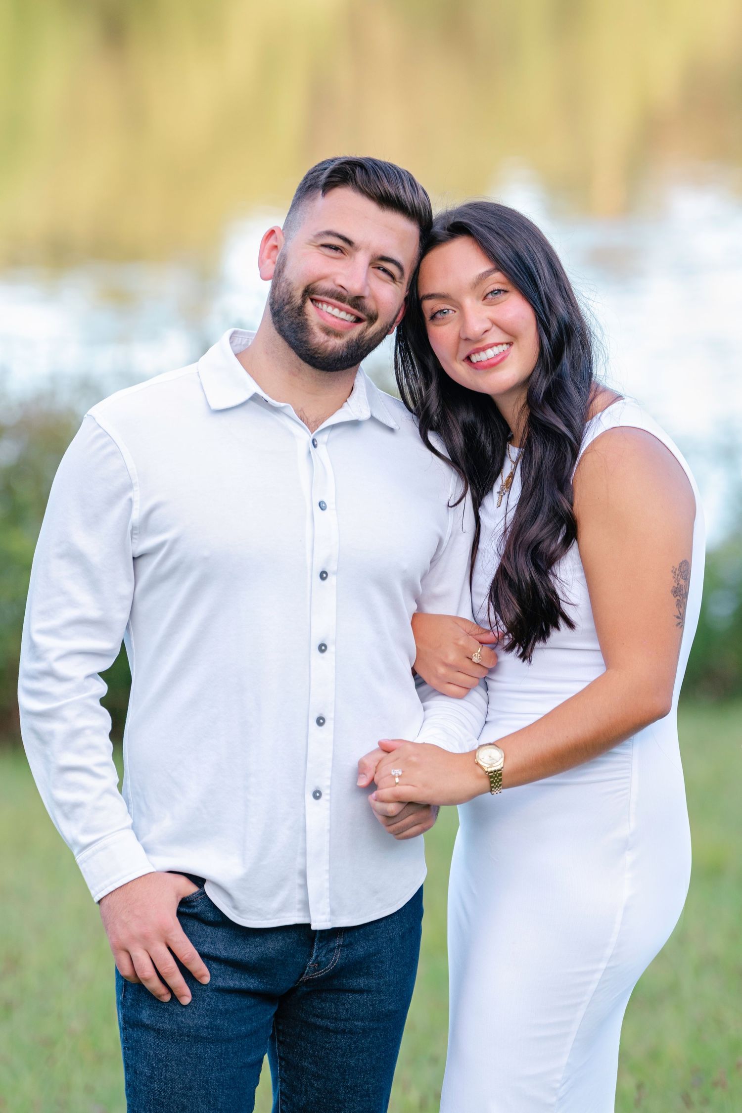 Romantic couple in white and denim share playful moments during an outdoor photoshoot in a grassy field.