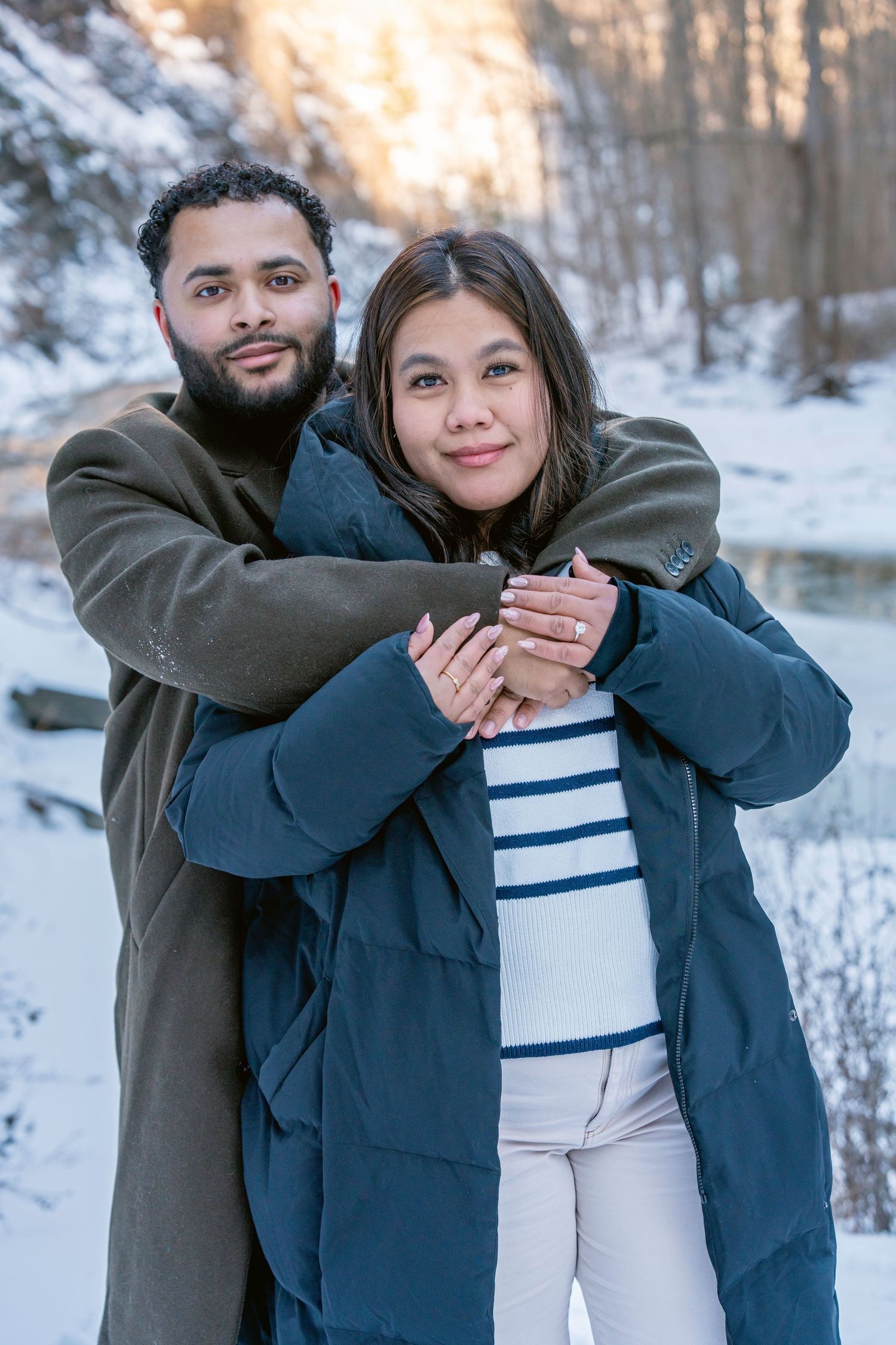 A couple embraces in a snowy winter landscape while wearing warm coats.