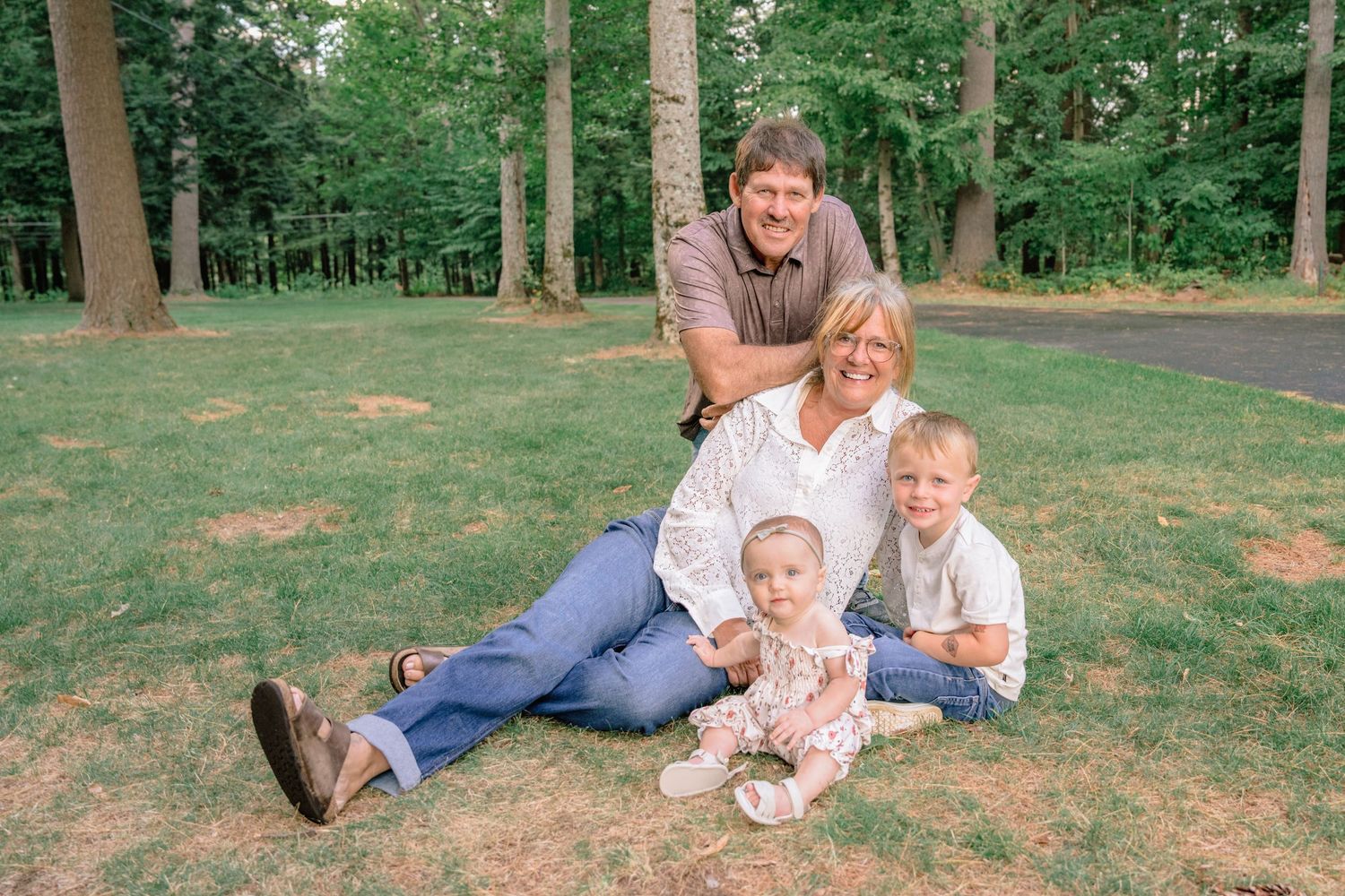 A family sits together on green grass in a wooded area during an outdoor photo session.