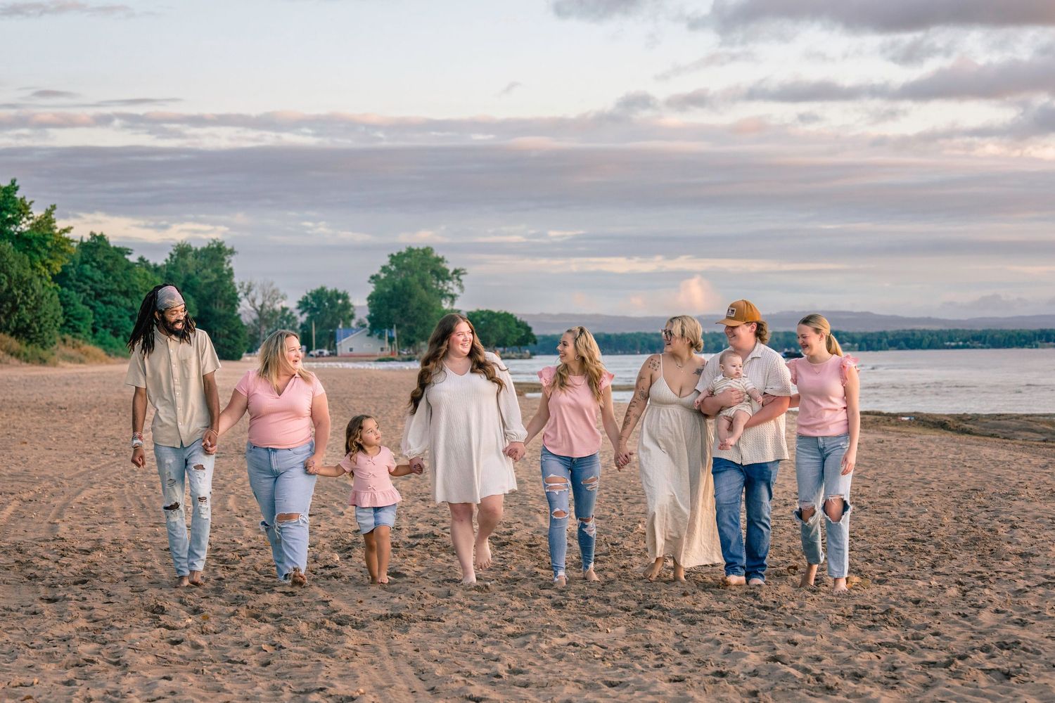 Group wearing coordinated pink and blue outfits walking along a beach at sunset holding hands.