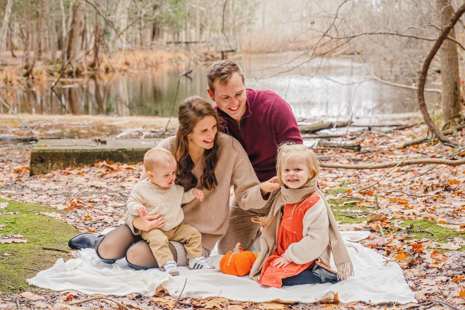 Family lying on white blanket surrounded by autumn leaves in outdoor photo session.