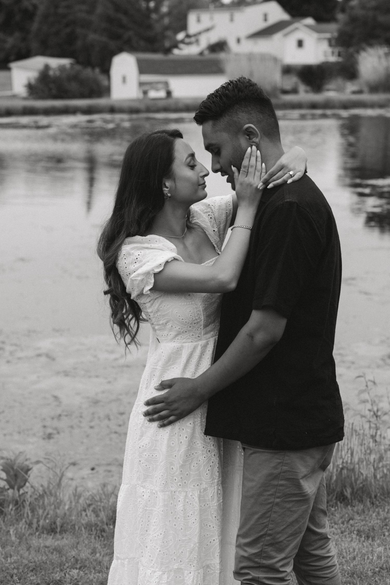 Romantic couple embraces by a serene lakeside in black and white photography.