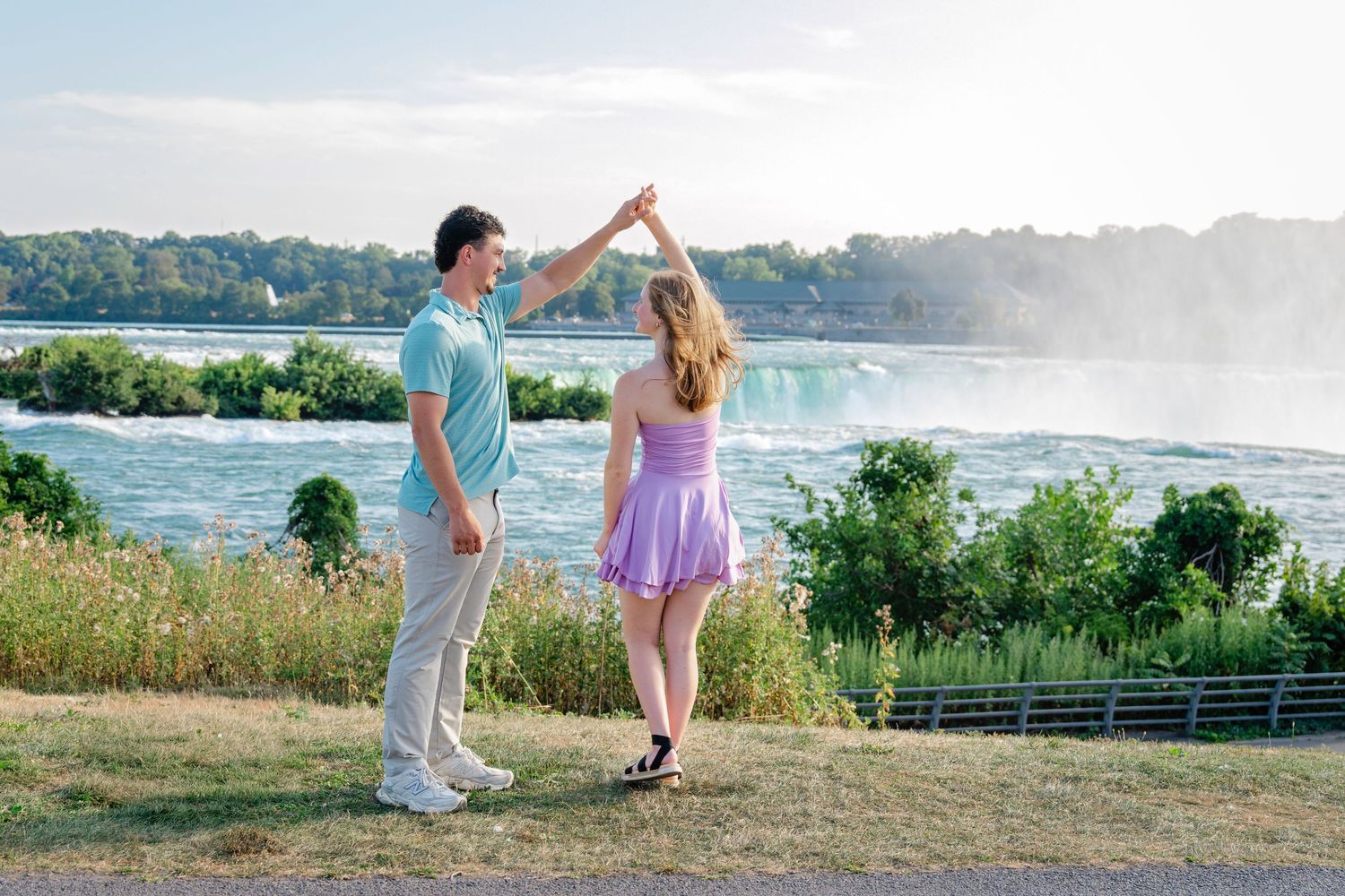 Couple dancing together near Niagara Falls with misty waterfall backdrop on a sunny day.