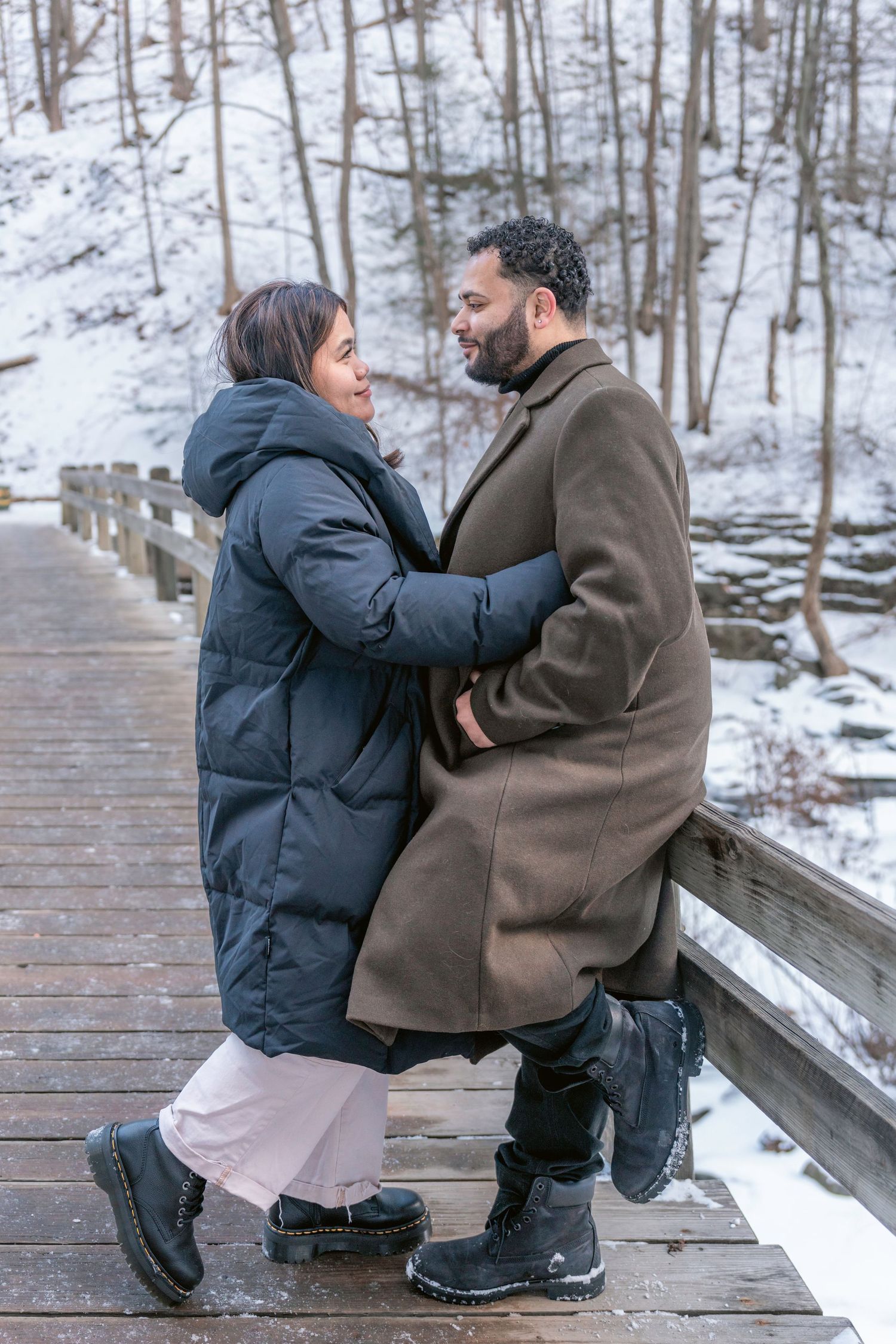 A romantic moment between two people on a wooden bridge surrounded by snowy winter scenery.