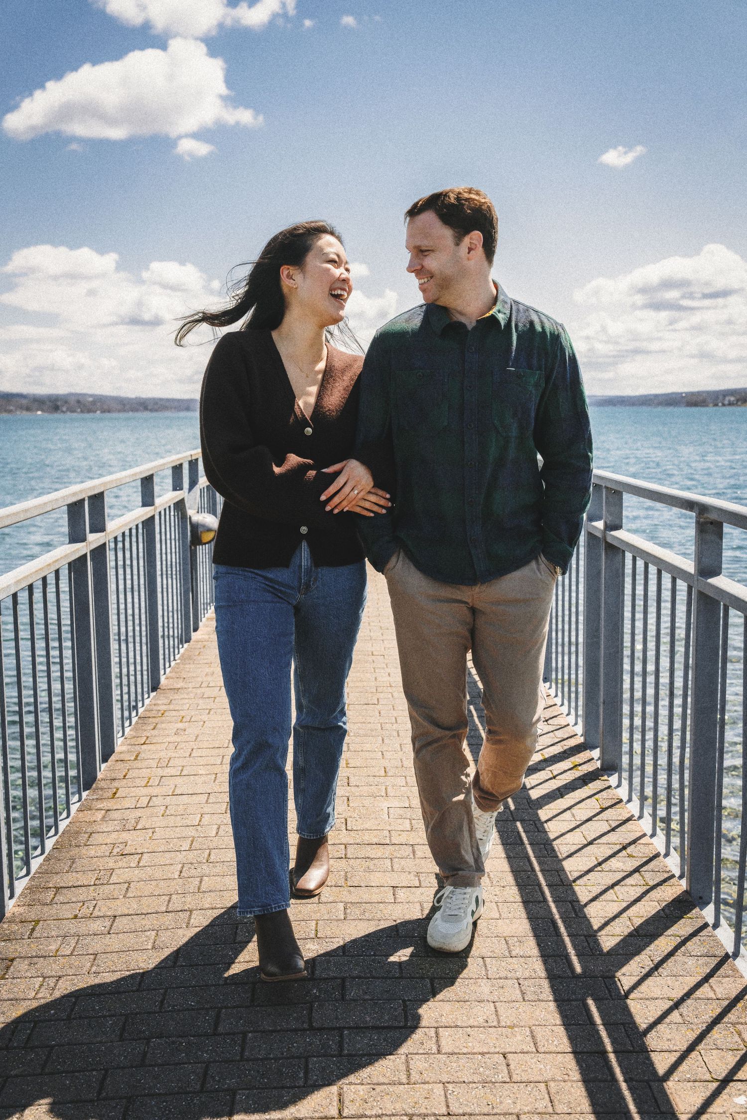 A couple walking and laughing together along a waterfront boardwalk with scenic water views.