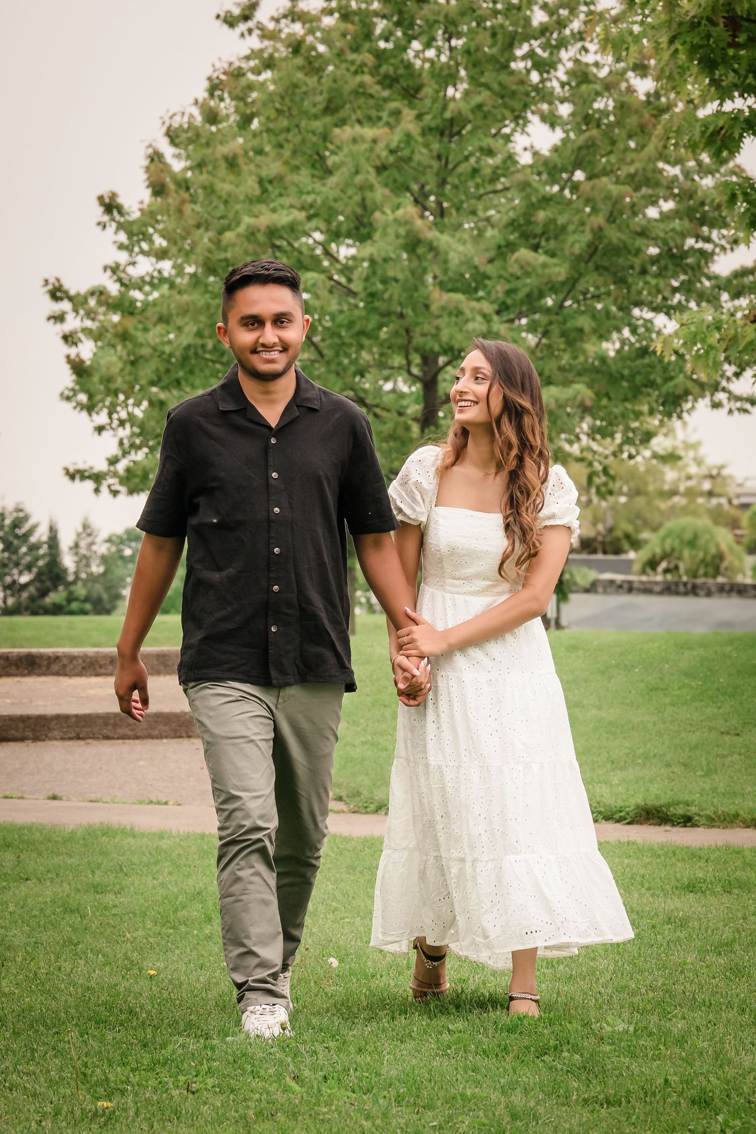 A couple walks together on a grassy lawn with trees in the background.