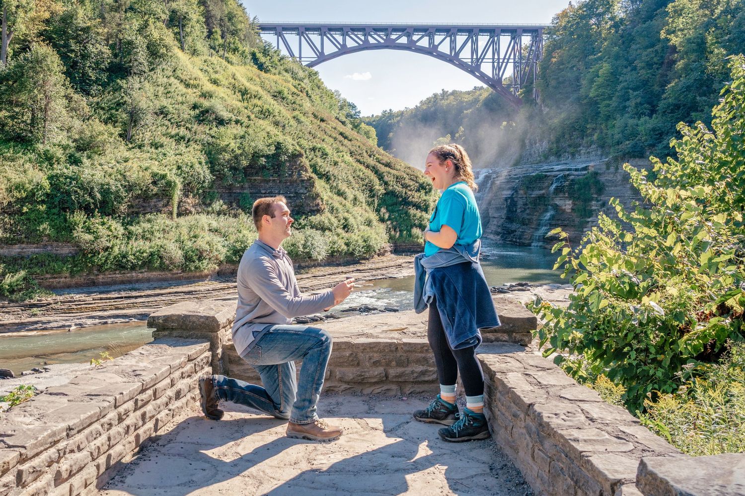 People enjoying scenic views from stone overlook near arched bridge at Letchworth State Park in New York.