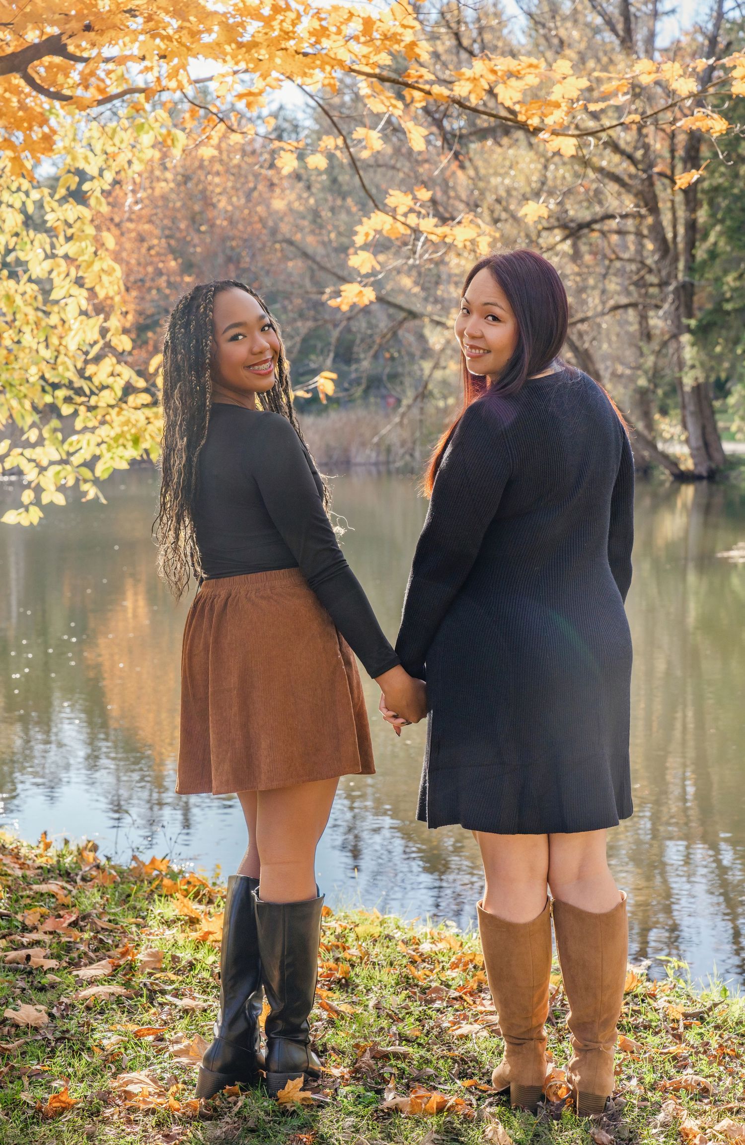 Two friends share a laugh while enjoying an autumn day by a tranquil lake surrounded by golden foliage.