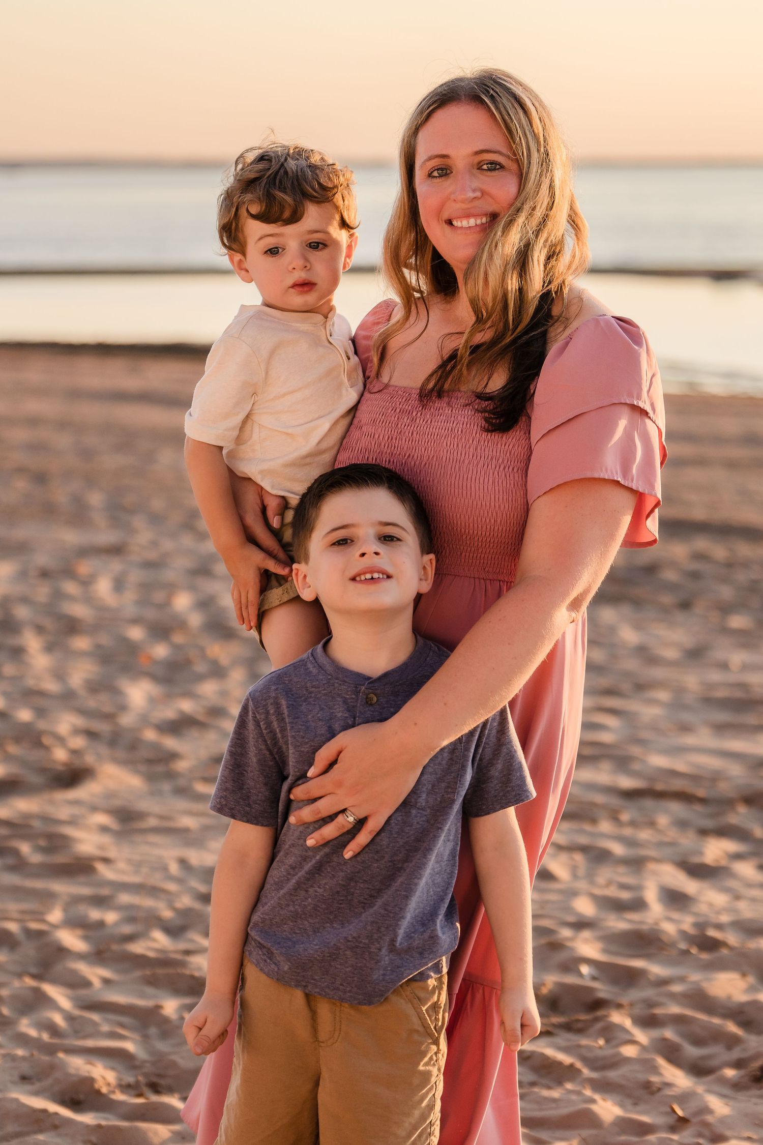 Family enjoying a sunset moment together on a sandy beach in warm golden light.
