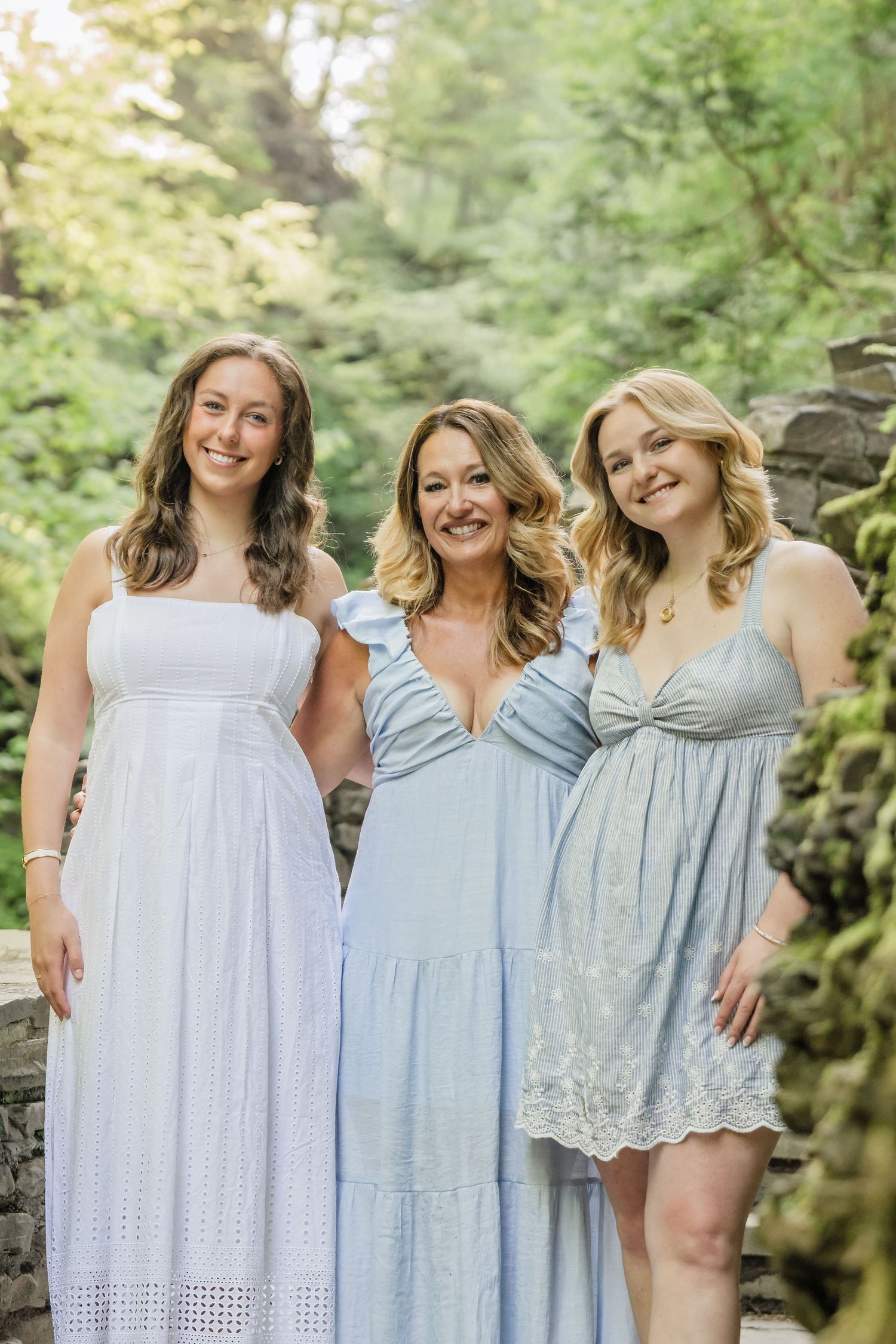 Group of friends wearing coordinated light blue and white summer dresses pose together in a garden setting.