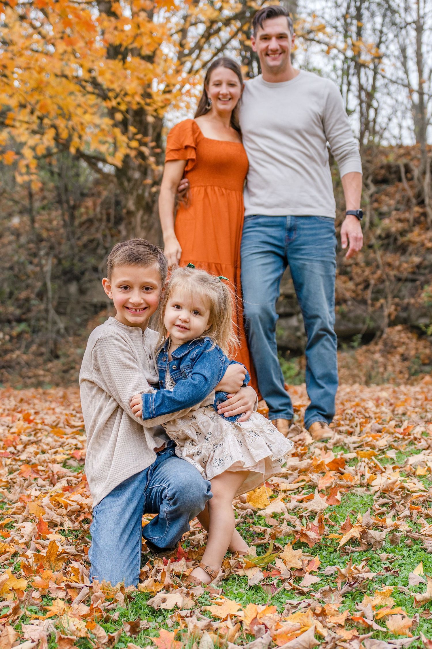 Family enjoying autumn day sitting together in colorful fallen leaves during outdoor photo session.