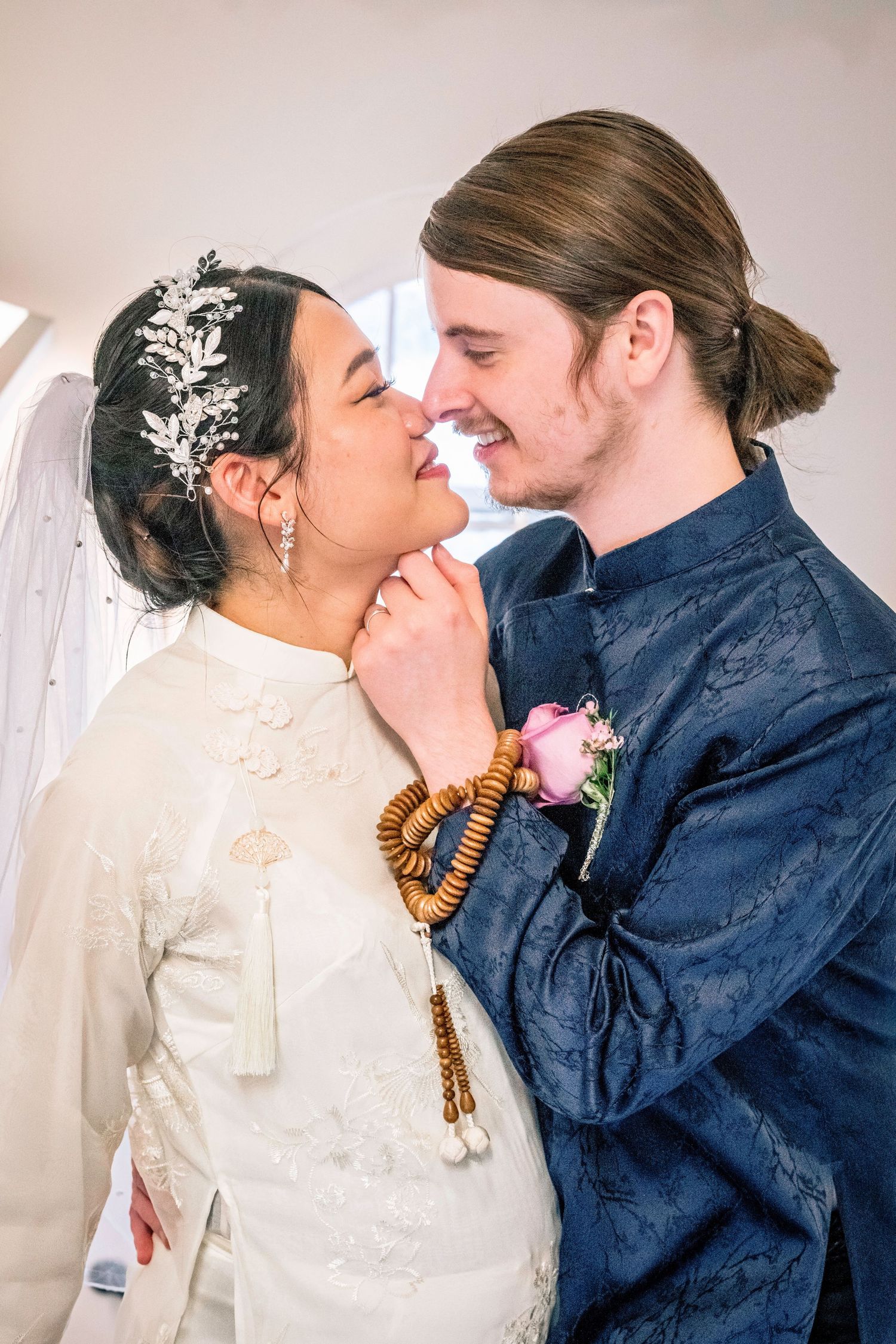 Interracial couple in traditional wedding attire sharing a romantic moment, bride in white ao dai with floral headpiece.