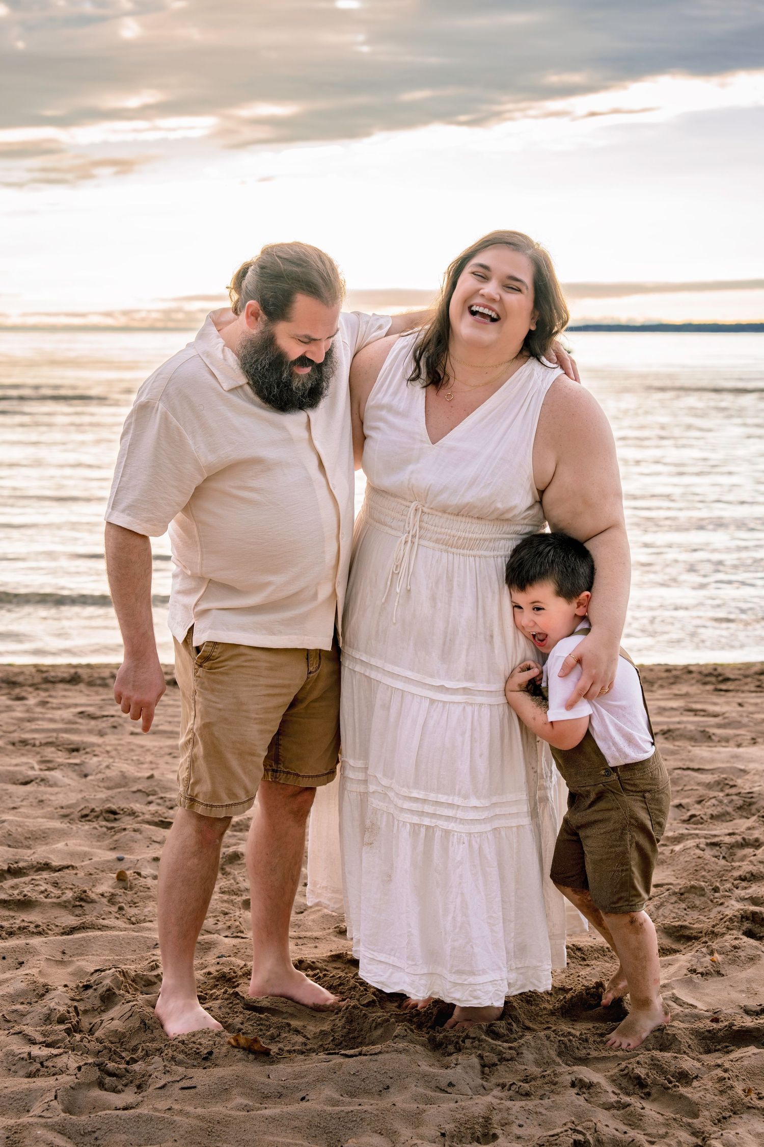 Family shares joyful moments together on sandy beach at sunset in coordinated white and tan outfits.