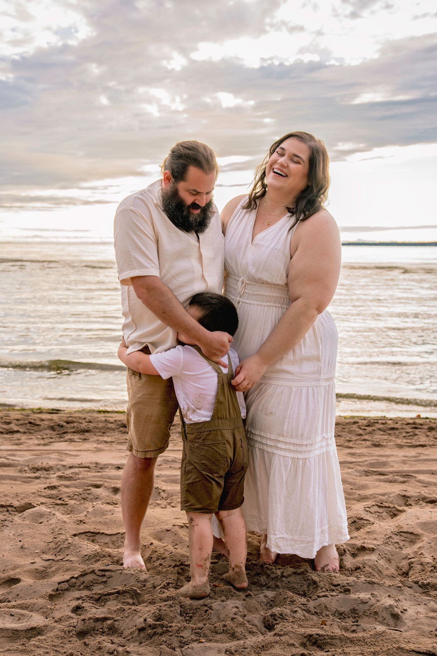 A family shares a joyful moment together on a sandy beach at sunset, laughing and embracing on the shoreline.