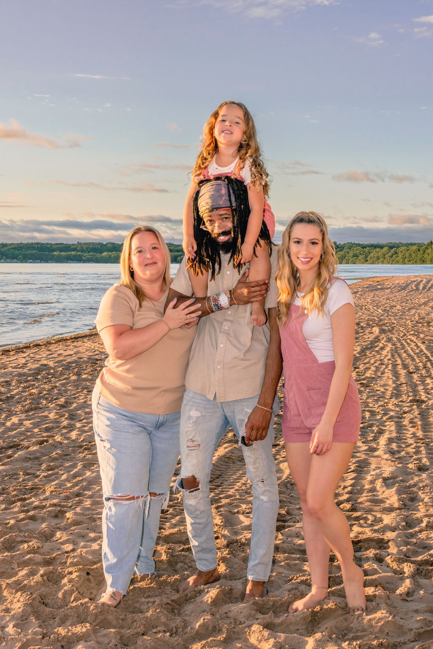 A group of friends pose together on a beach at sunset with the ocean and sky in the background.