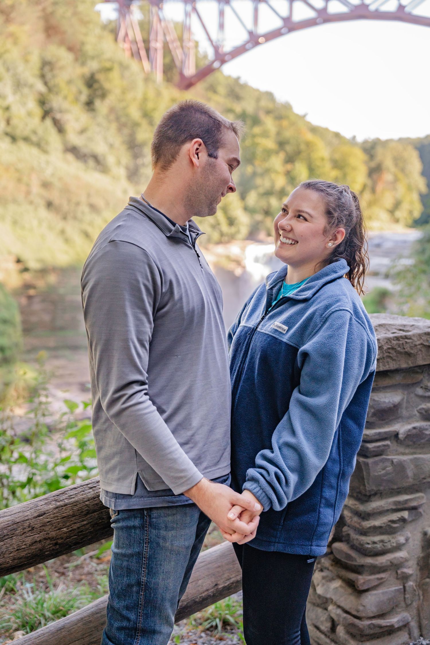 A couple shares a romantic moment together on a stone wall in an autumn outdoor setting.