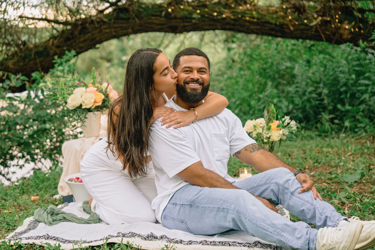 Romantic outdoor picnic scene with couple relaxing on blanket surrounded by greenery.