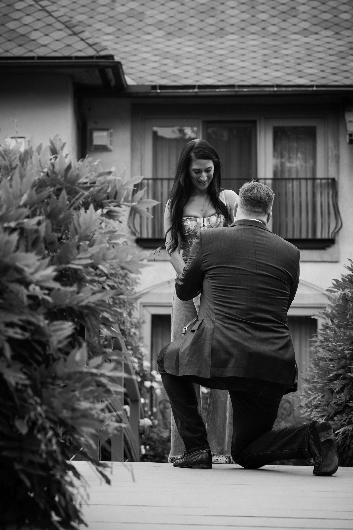 A series of black and white photos showing a proposal sequence on a front porch with decorative greenery.
