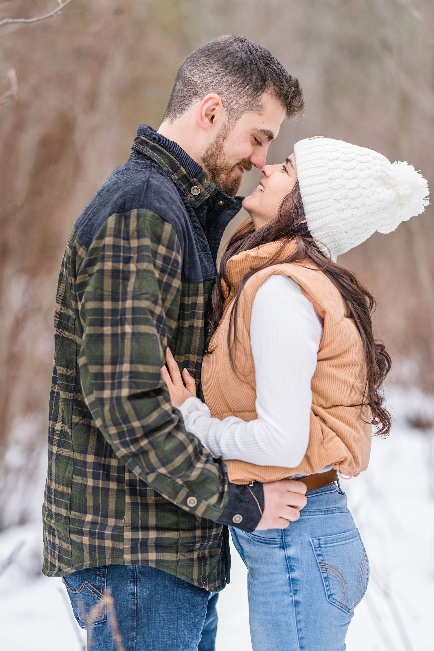 A couple embraces in a romantic winter scene wearing casual clothing against a snowy outdoor backdrop.