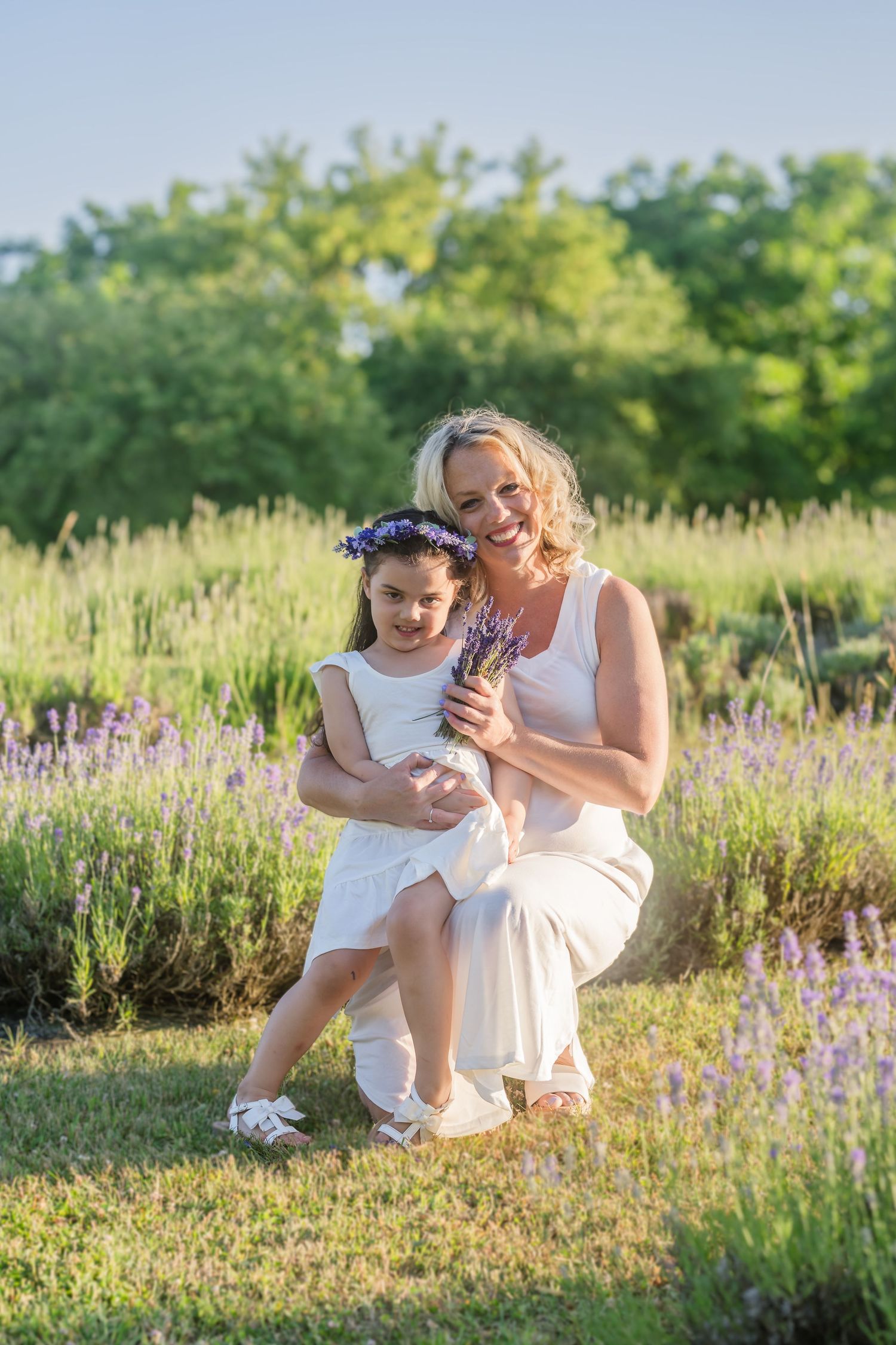 Two people share a tender moment together while sitting in a field of purple wildflowers at sunset.
