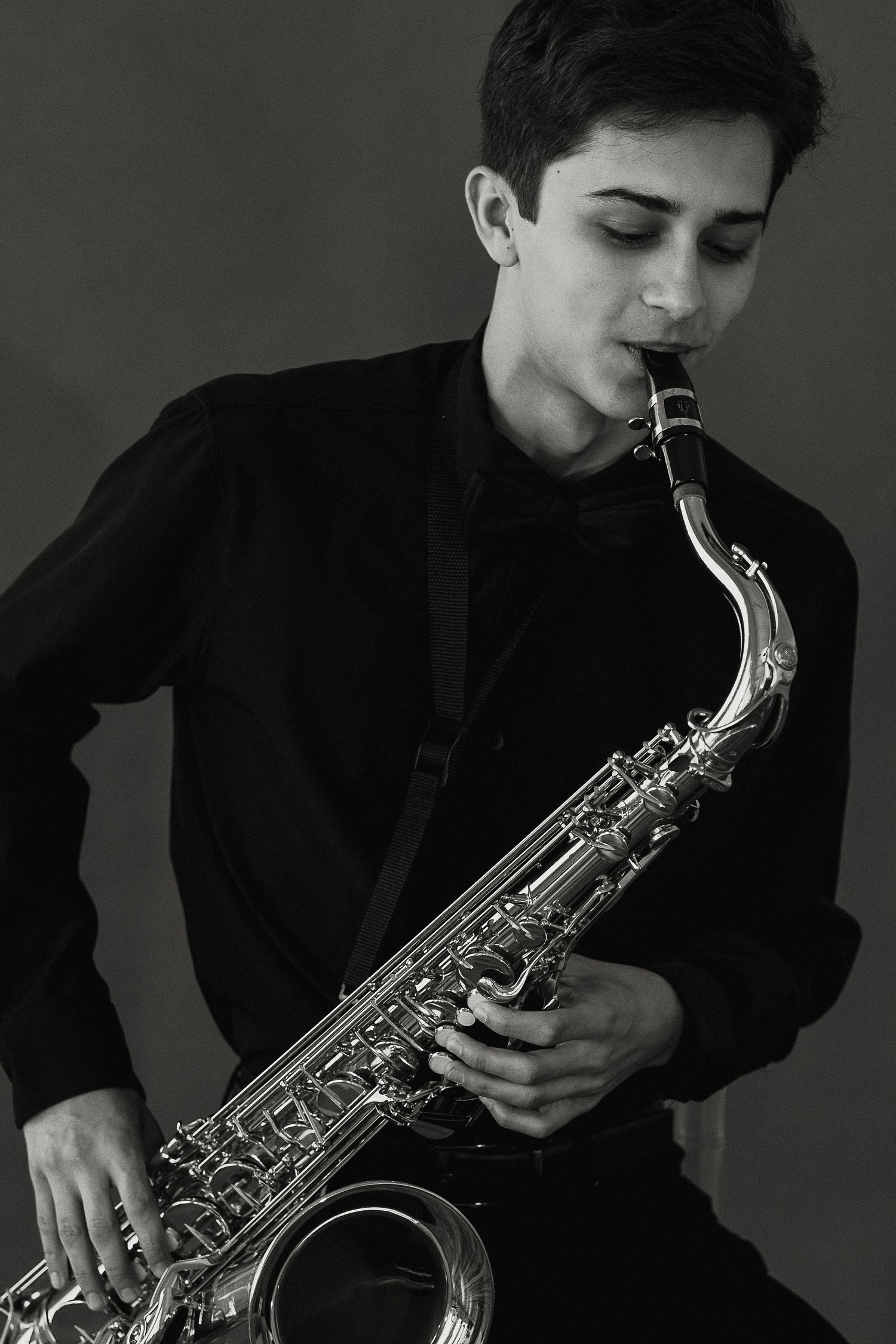 Senior portrait black and white portrait of a musician playing saxophone while wearing dark formal attire.