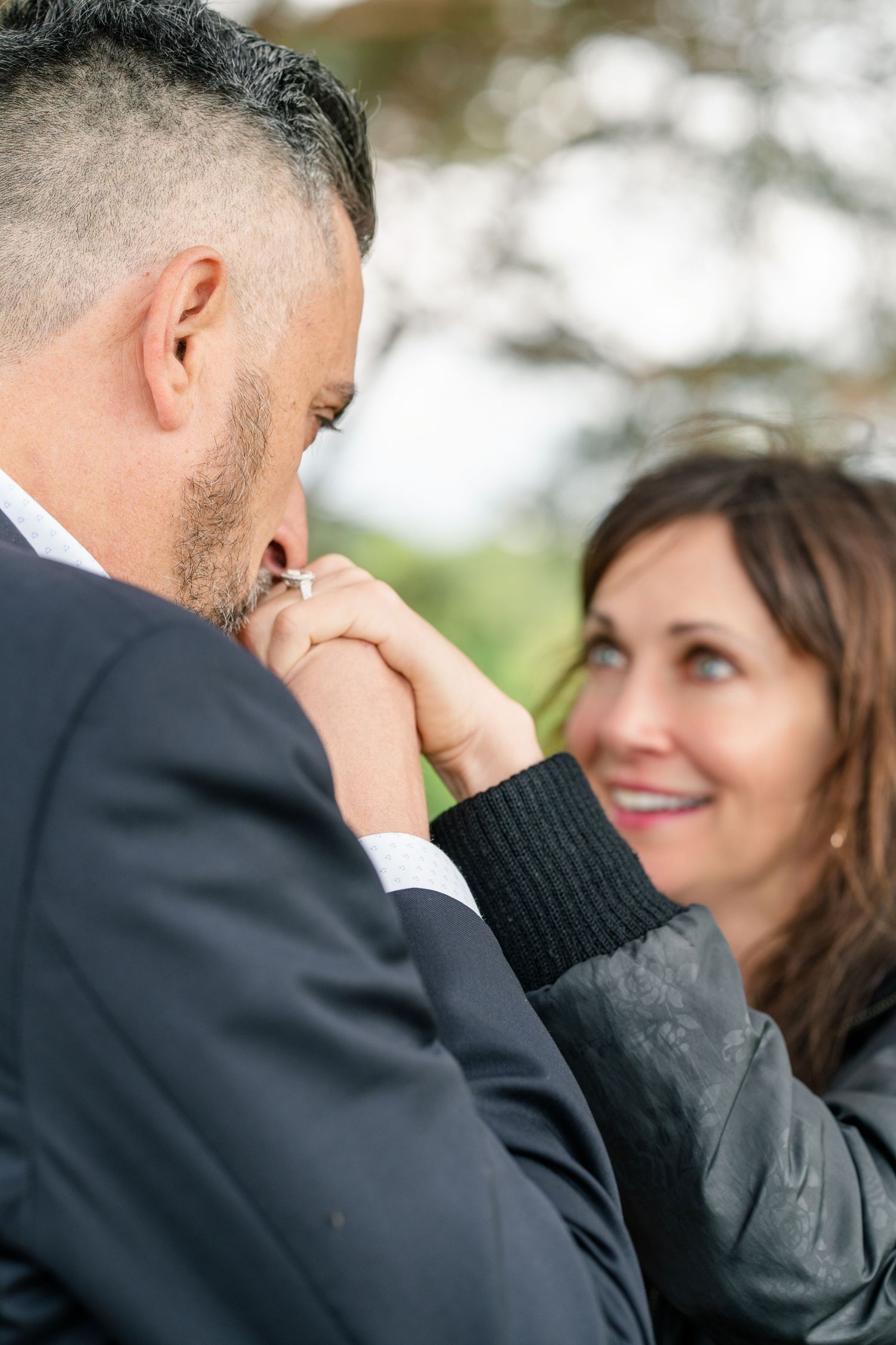 A romantic outdoor moment between a couple as they share a tender gesture with soft bokeh lighting in the background.