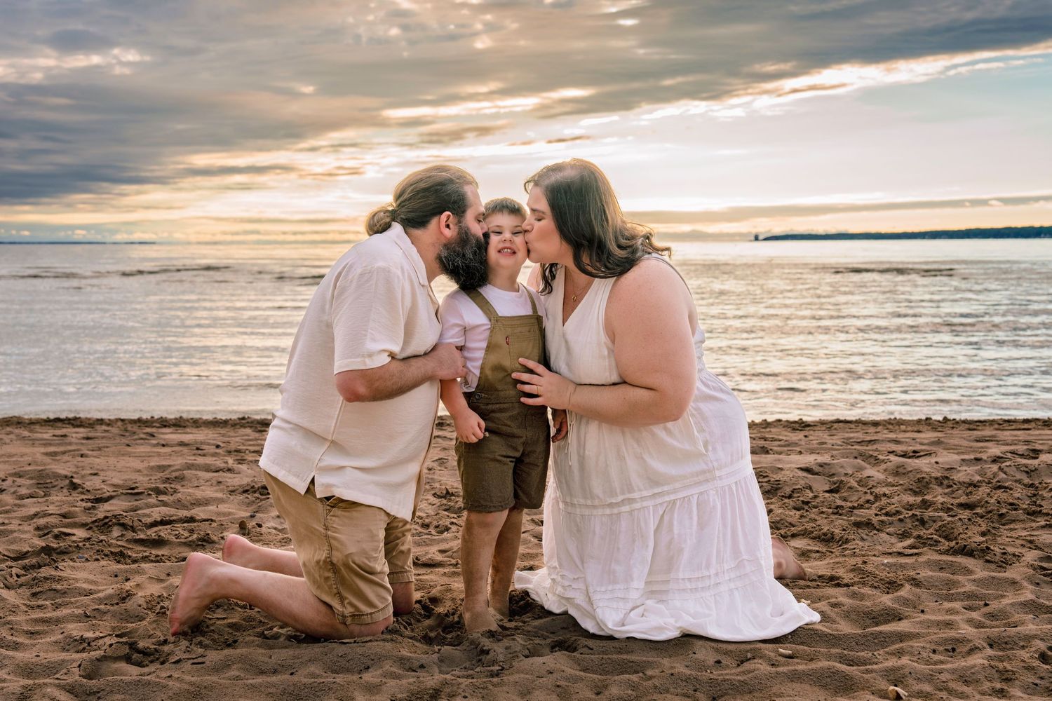 Family enjoying a sunset photo session together on a sandy beach with golden light reflecting off the ocean.