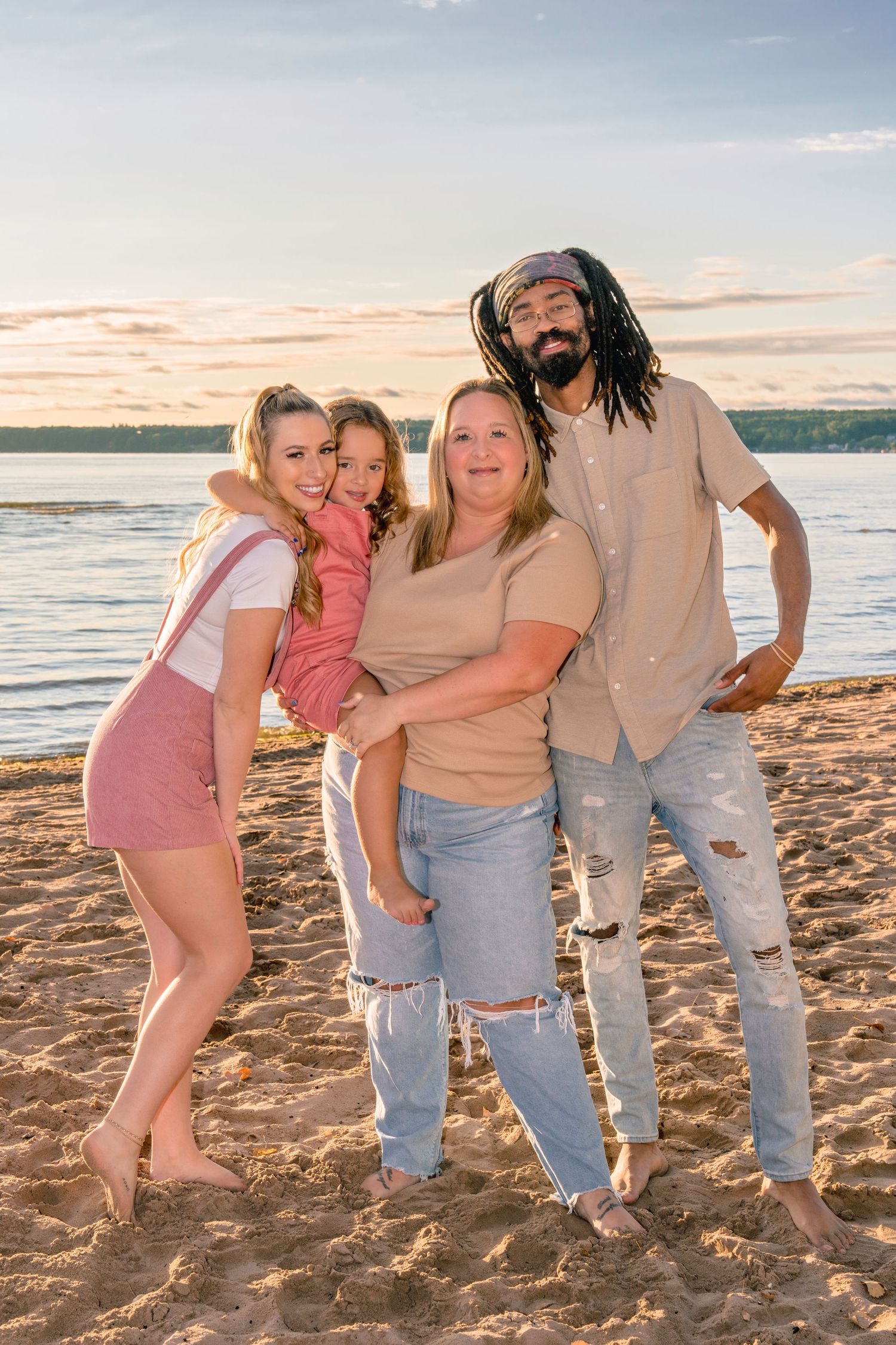 A playful group poses together on a sandy beach during golden hour with the ocean waves in the background.