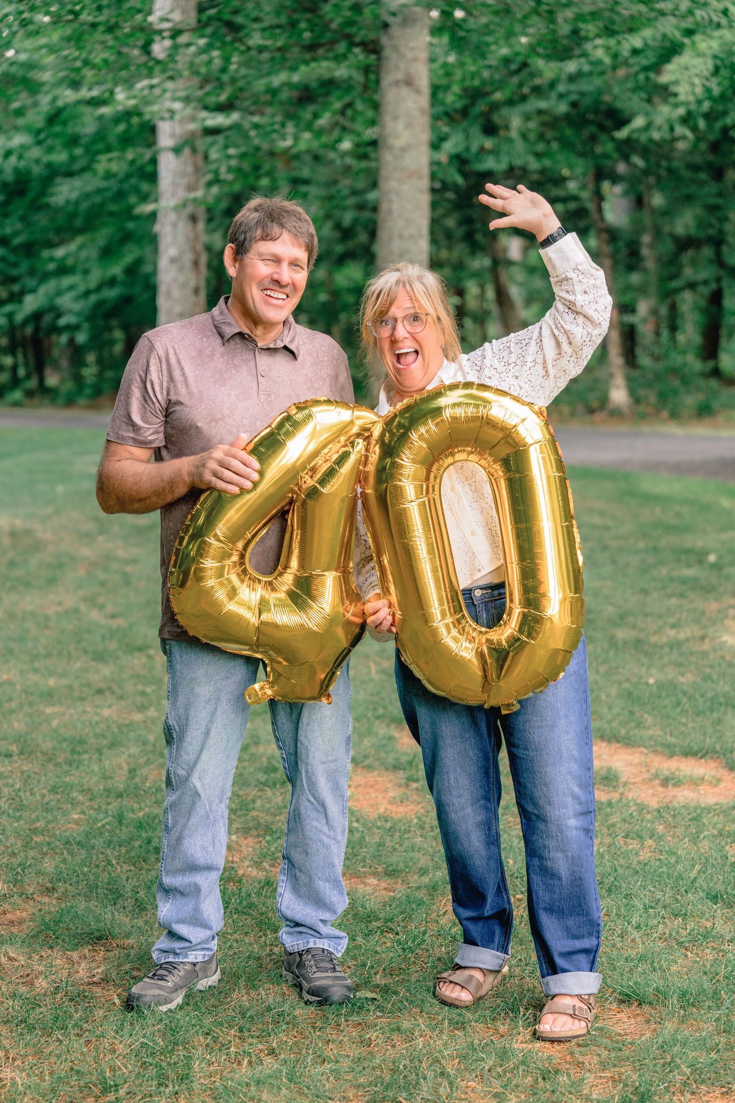 Two people holding large gold number 40 balloons stand together in a grassy outdoor setting.