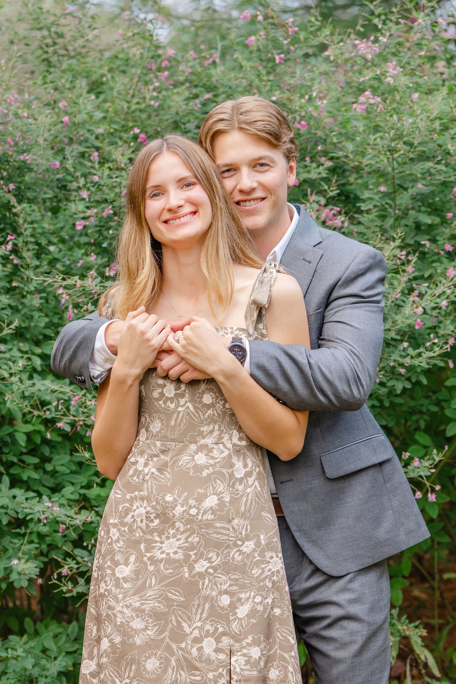 A couple poses together outdoors in a garden with pink flowers, wearing formal attire and embracing in a series of candid moments.